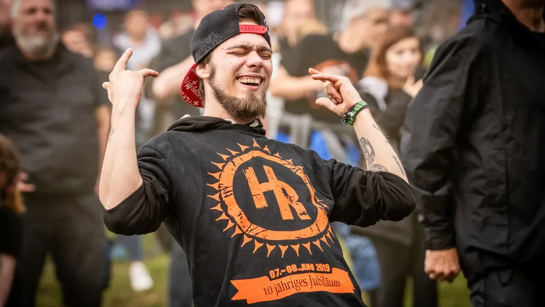 Festivalgast mit Kappe und Holtebüttel-Rockt-Shirt zeigt mit beiden Händen das Rockzeichen beim Pre-Opening 2025
