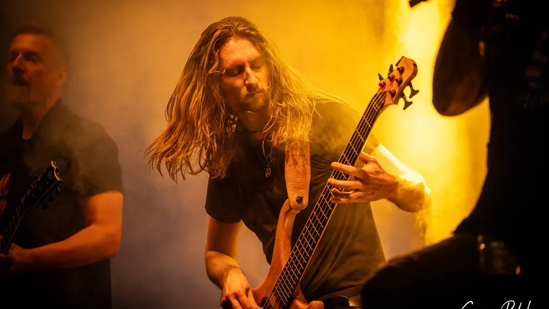 Bassist mit langen Haaren im gelben Bühnenlicht, Holtebüttel Rockt 2024
